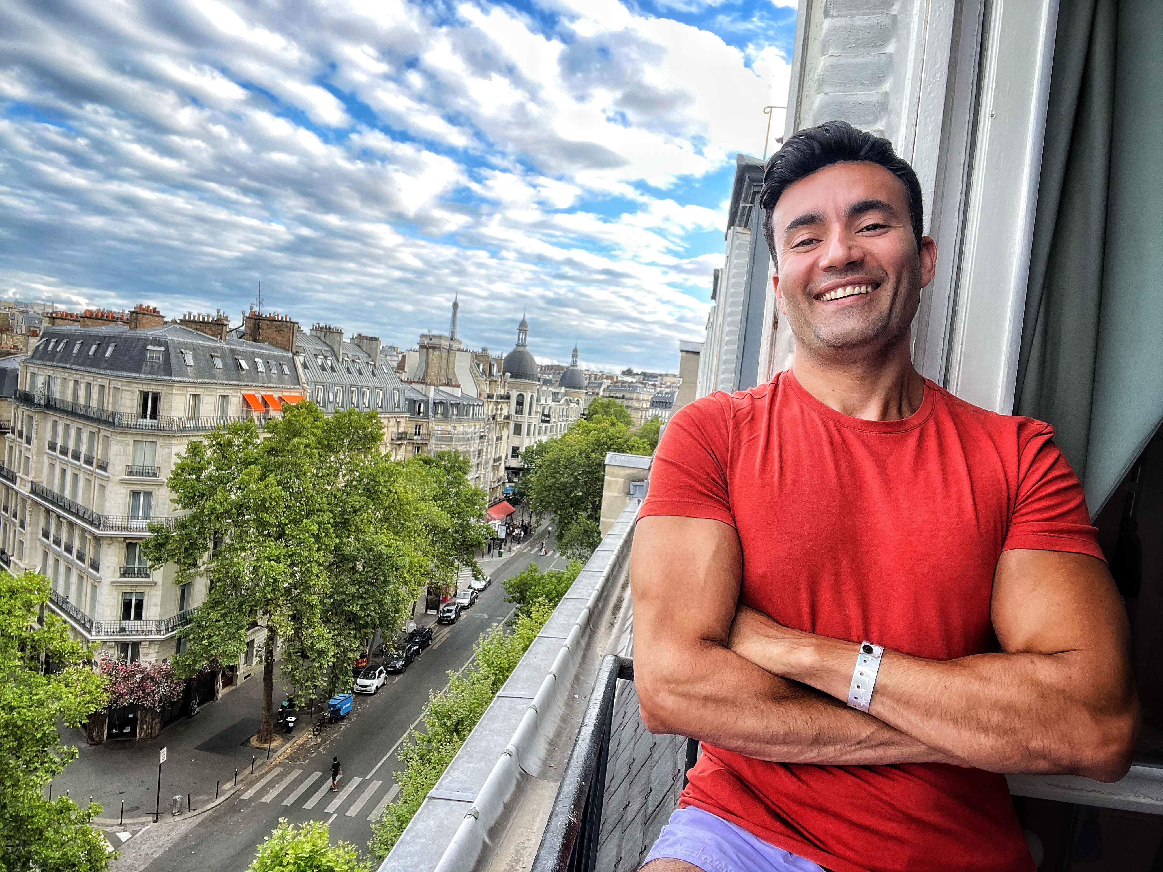 Aladdin Ismail on a Paris balcony in a red t-shirt, Haussmann rooftops behind him